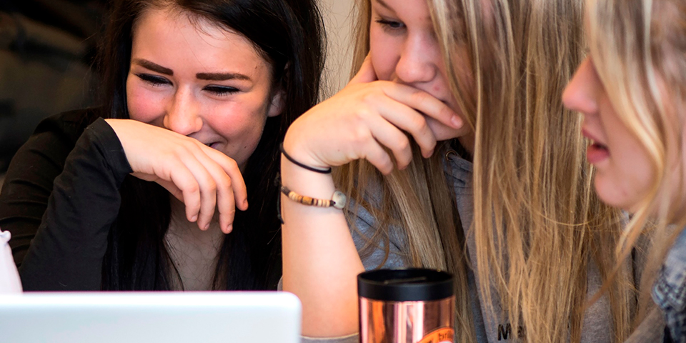 Tre piger sidder sammen og griner, mens de kigger på den samme computer