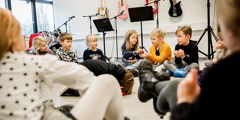 Børn sidder i en rundkreds til musikundervisningen