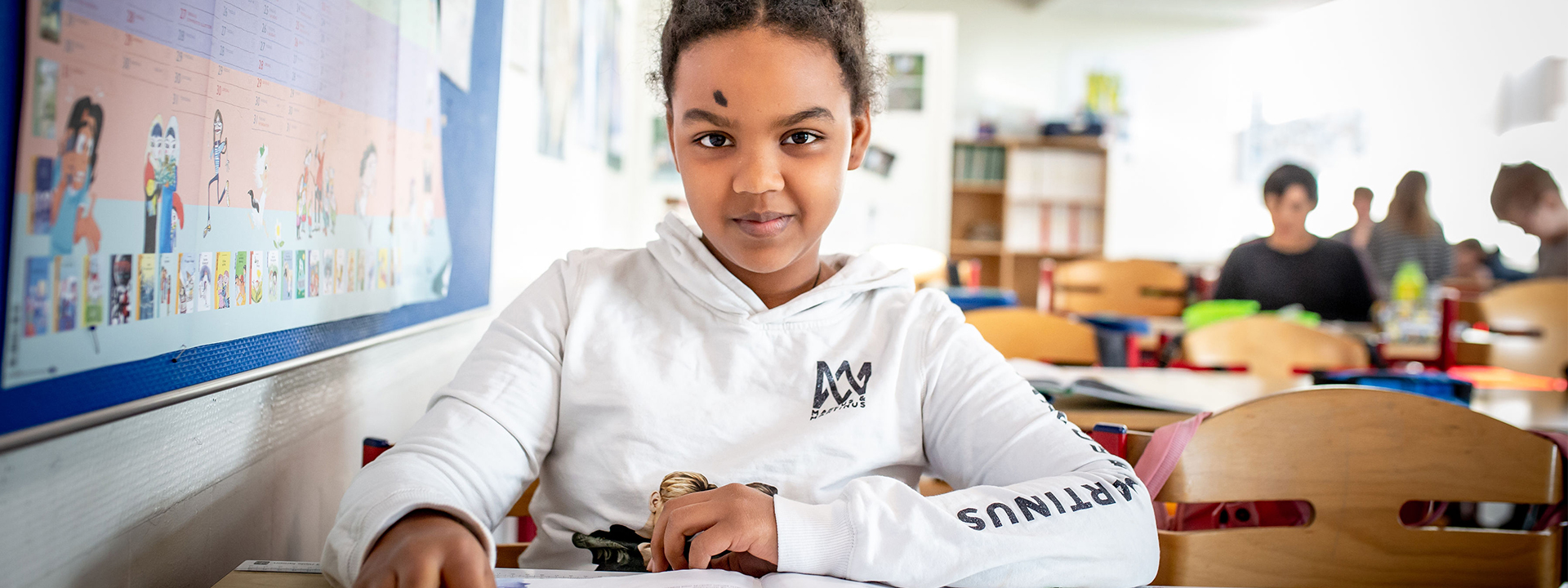 Pige sidder i klasselokale og kigger ind i kameraet